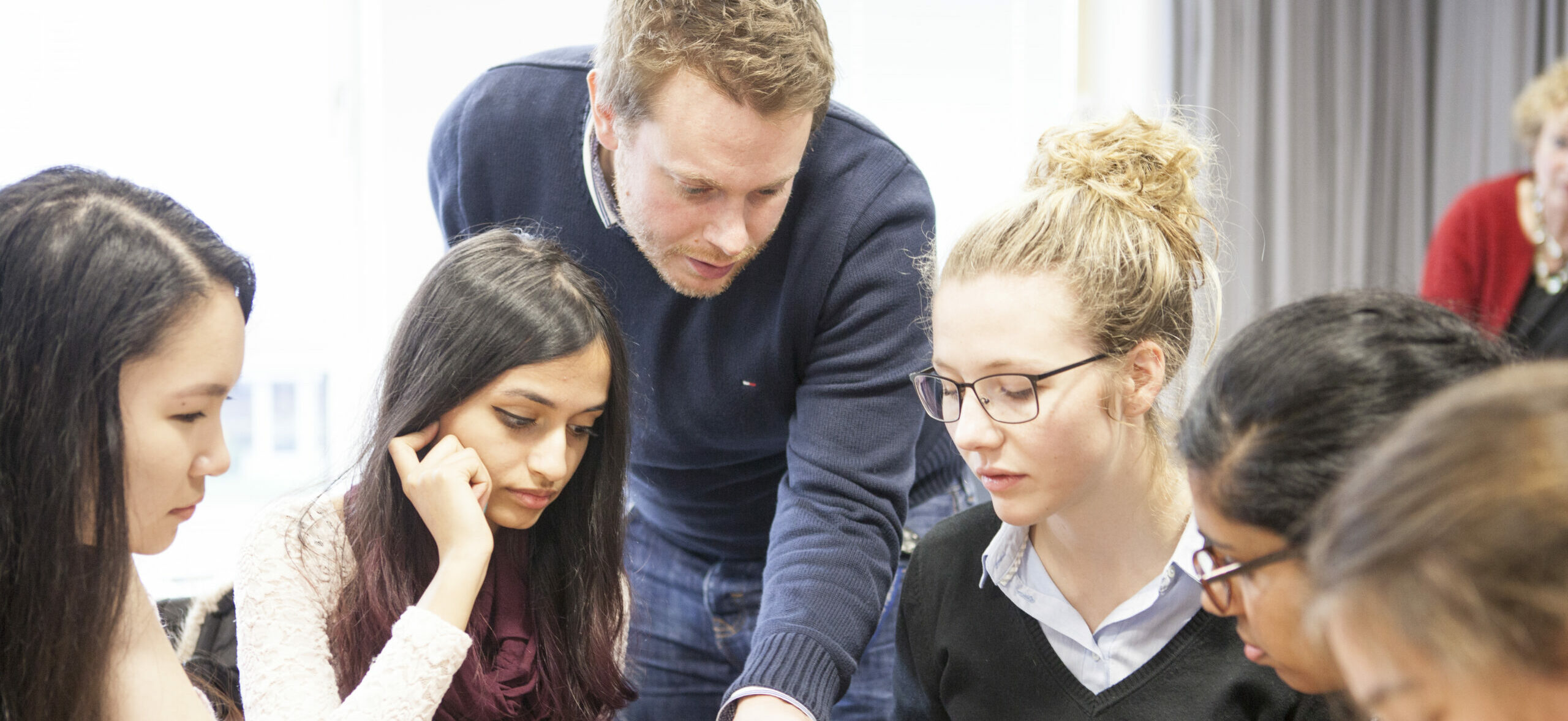 Eine Gruppe von fünf Menschen arbeitet zusammen. Eine Lehrperson erklärt ihnen etwas.