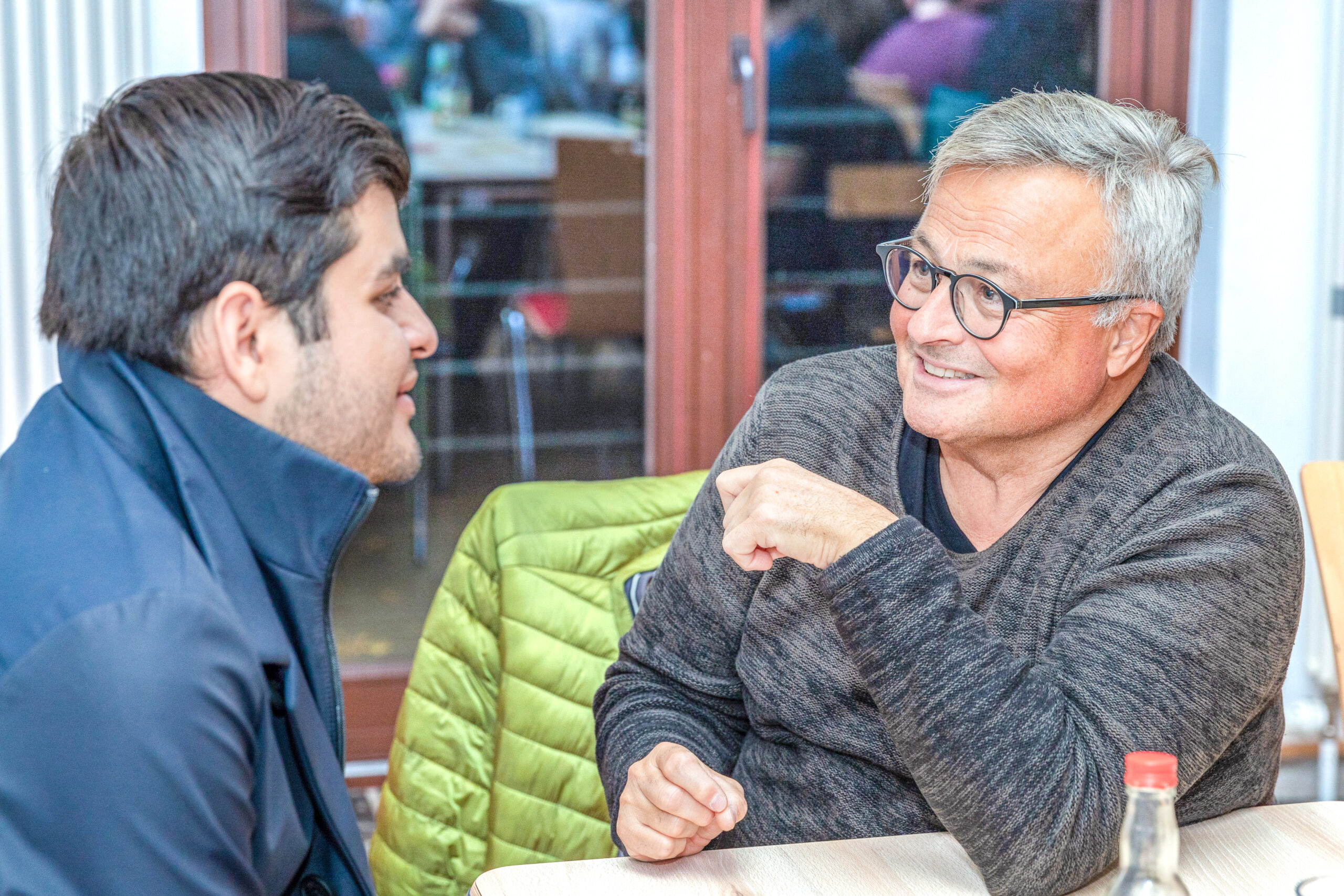 Zwei Männer sitzen sich gegenüber und unterhalten sich angeregt. Two men are sitting opposite each other and talking animatedly.